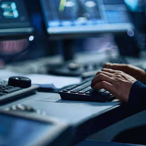Hands on a keyboard at an operations console with multiple monitors in low light